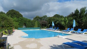 A swimming pool with blue lounge chairs and umbrellas, surrounded by greenery. - 7 Gîtes in 100 acres with heated pool. Near Pont Aven, Concarneau, beaches 15km (Bretagne)