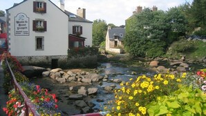 A white building with a sign reading "Boutique du Grand Poulin" and a river with rocks and flowers in front. - 7 Gîtes in 100 acres with heated pool. Near Pont Aven, Concarneau, beaches 15km (Bretagne)