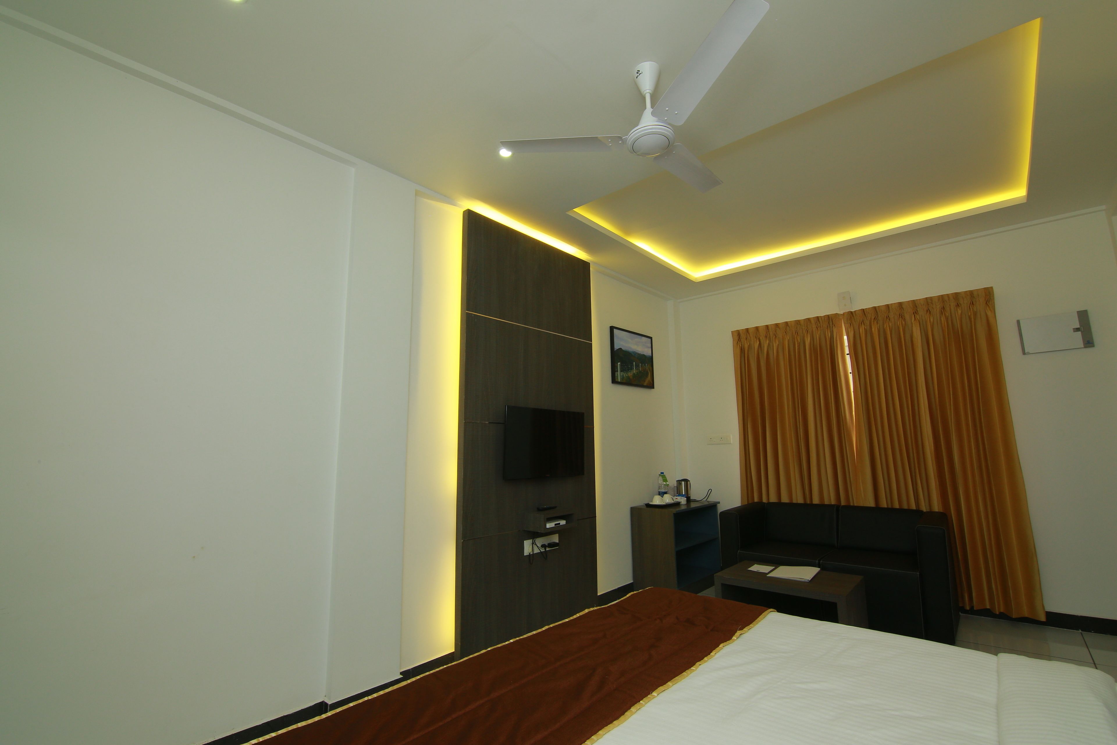 A hotel room with a bed, a ceiling fan, a TV, a desk, and a window with curtains.