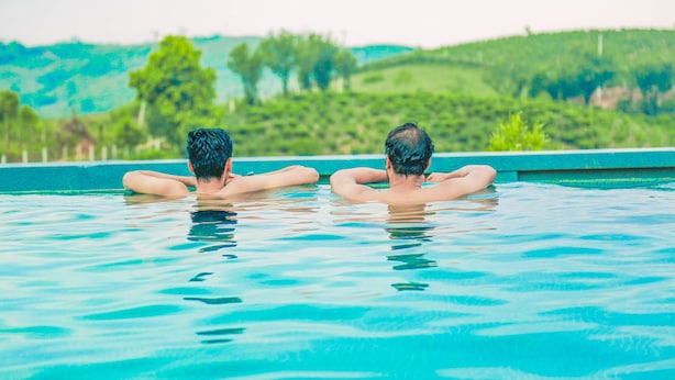 Two people relaxing in a swimming pool with a view of green hills in the background. - Palette Hill View Resort Vagamon (Peermade)