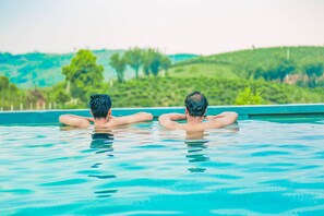 Two people relaxing in a swimming pool with a view of green hills in the background. - Palette Hill View Resort Vagamon (Peermade)