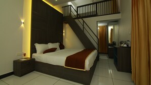 A modern bedroom with a large bed, a nightstand, a desk, and a staircase leading to an upper level. - Palette Hill View Resort Vagamon (Peermade)