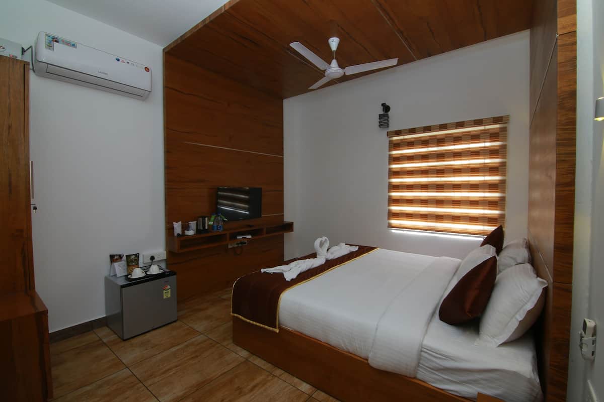 A hotel room with a bed, a ceiling fan, a TV, a small desk, and a window with blinds.