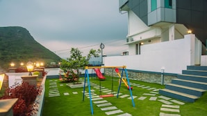 A modern building with a staircase leading to a balcony, a swing set, and a red slide in a landscaped backyard. - Palette Hill View Resort Vagamon (Peermade)