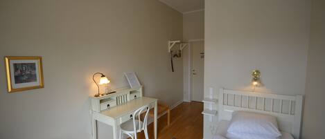 Un dormitorio con cama, escritorio, silla, un tapete pequeño y una lámpara fijada a la pared.