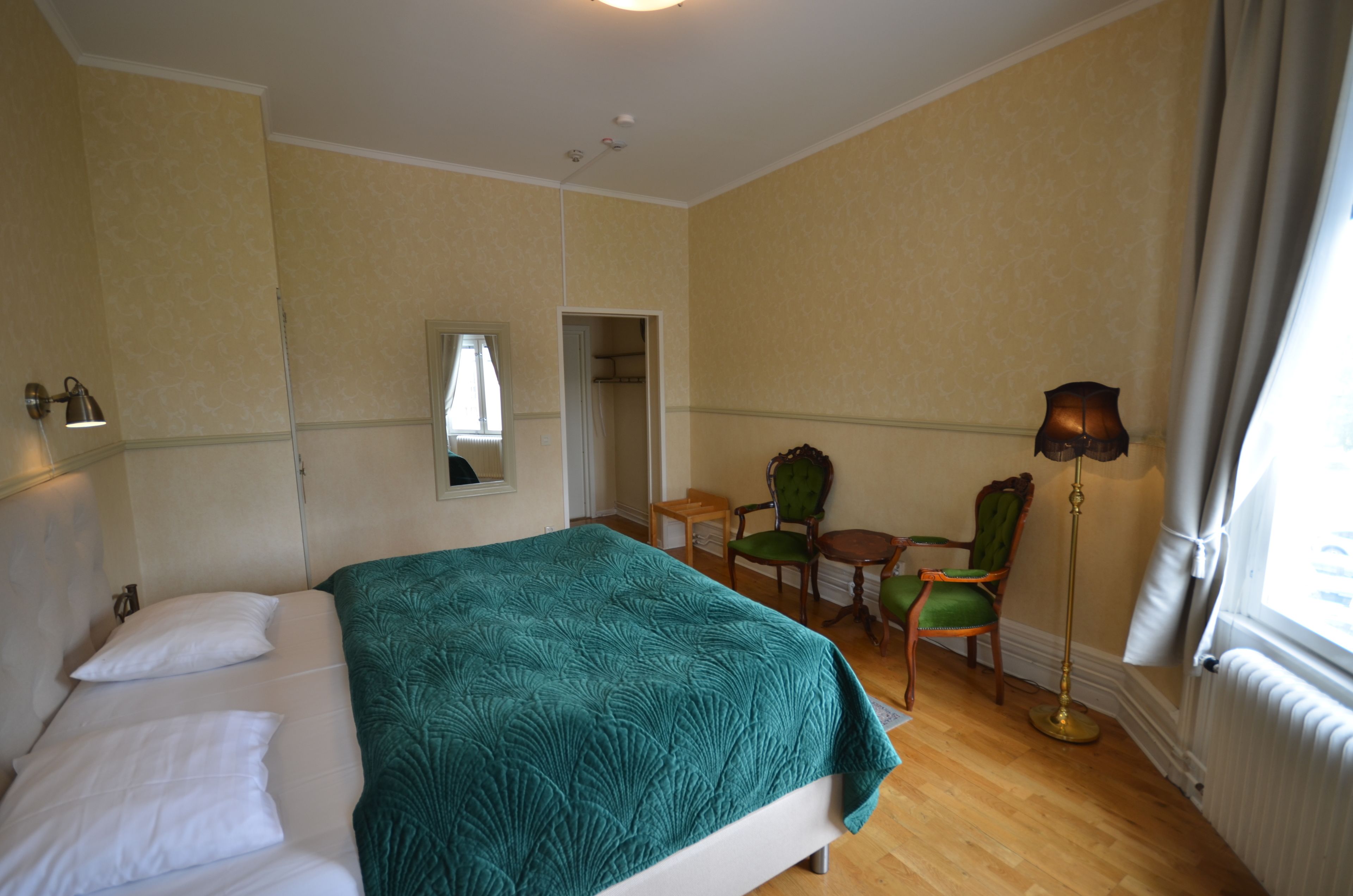 Una habitación de hotel con cama, escritorio, dos sillas, lámpara y ventana.
