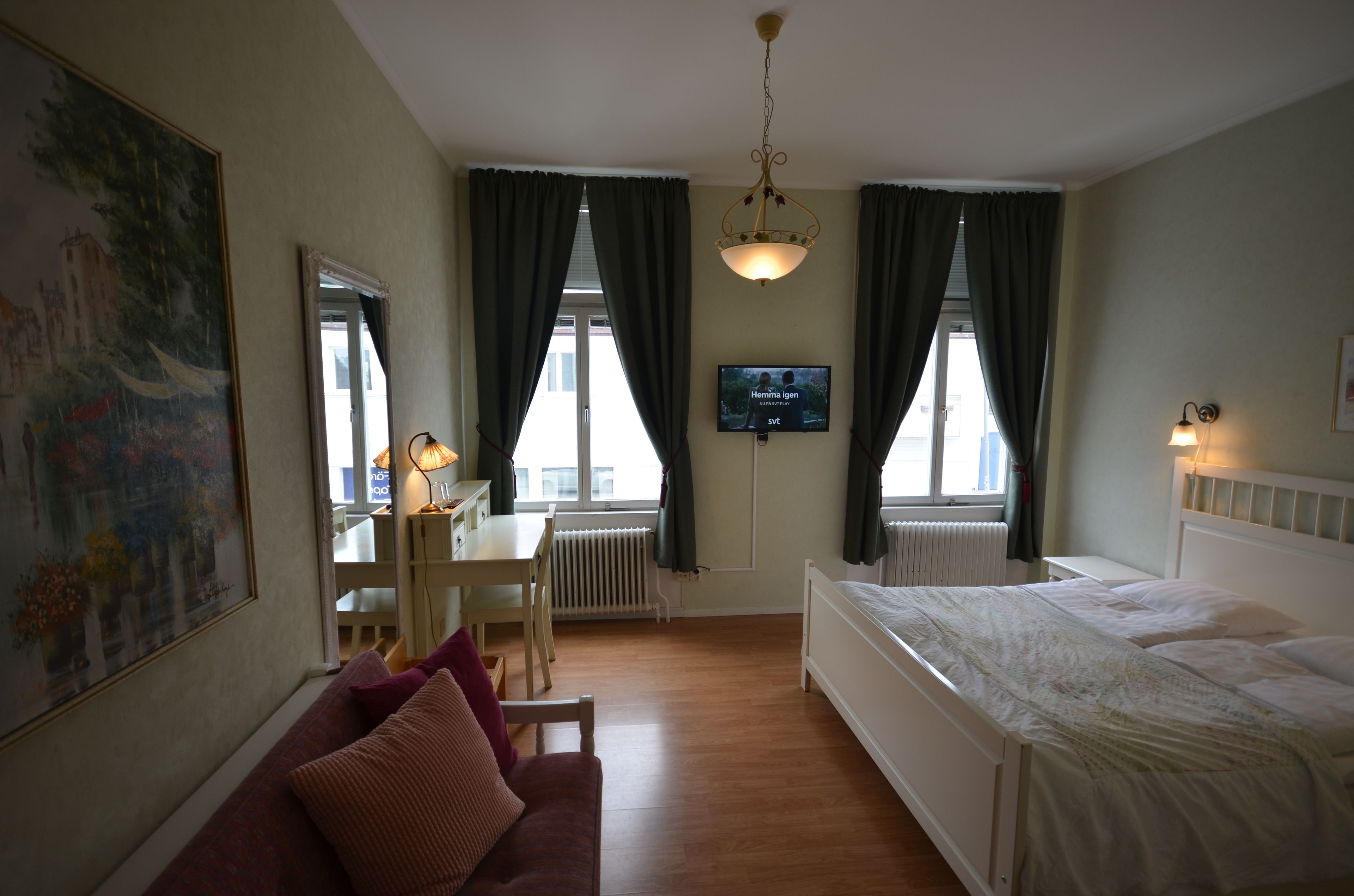 A hotel room with a bed, a desk, a chair, a sofa, a TV, and a painting on the wall.