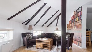 A modern living room with exposed wooden beams, a sofa set, a coffee table, and a bookshelf. - Hotell Royal (Harnosand)