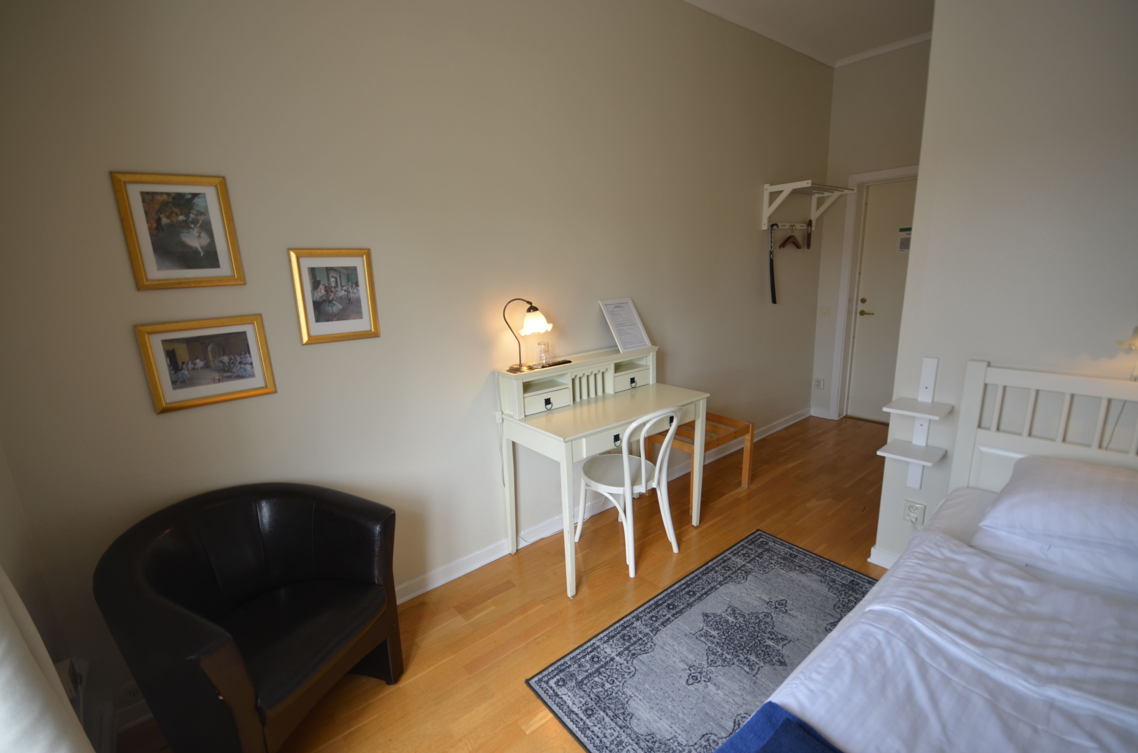 Quarto com uma cama, escrivaninha com cadeira, poltrona de couro preta e uma mesinha com abajur.