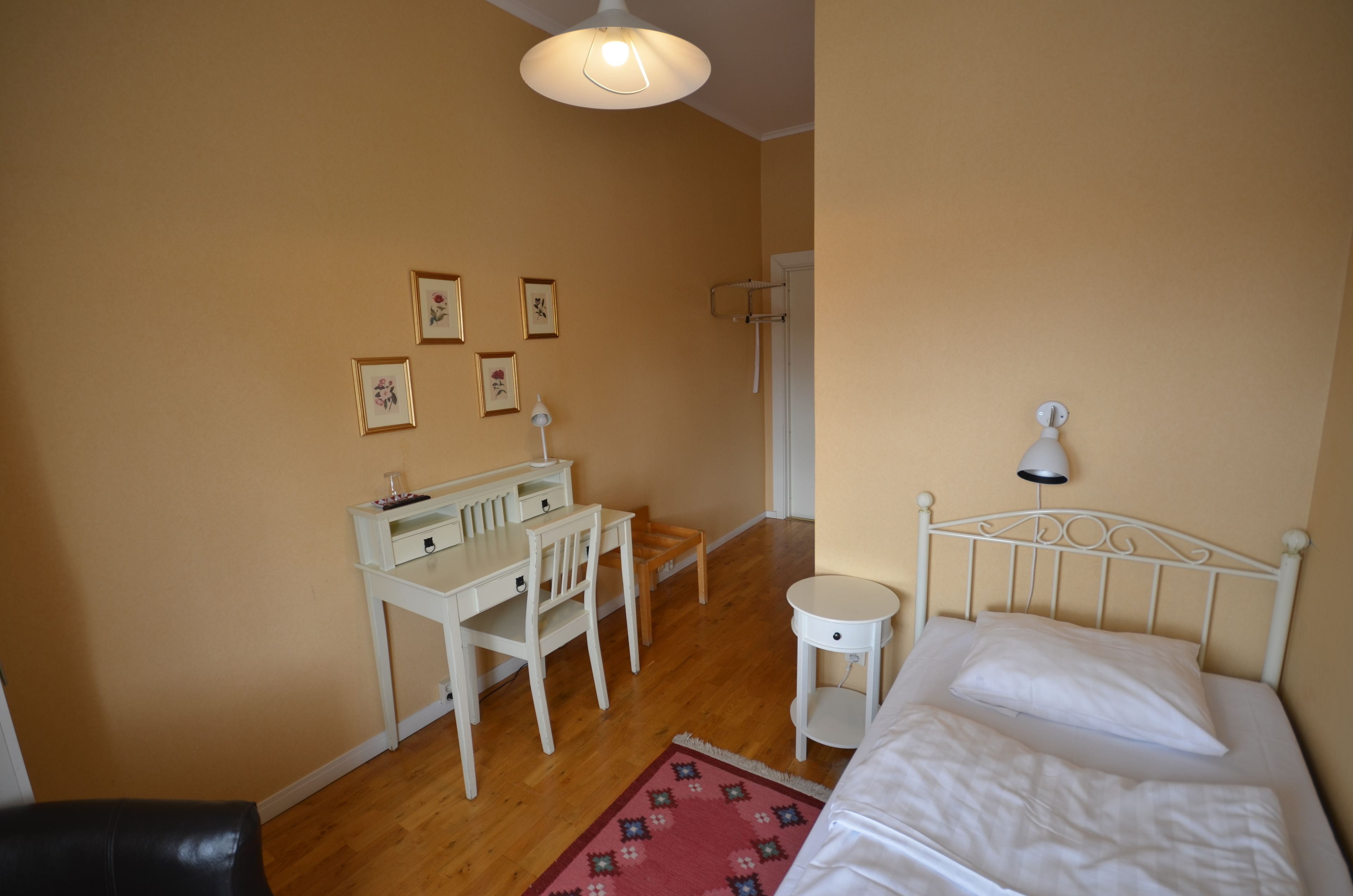 Un dormitorio con cama, escritorio, silla, mesita y una lámpara de pared.