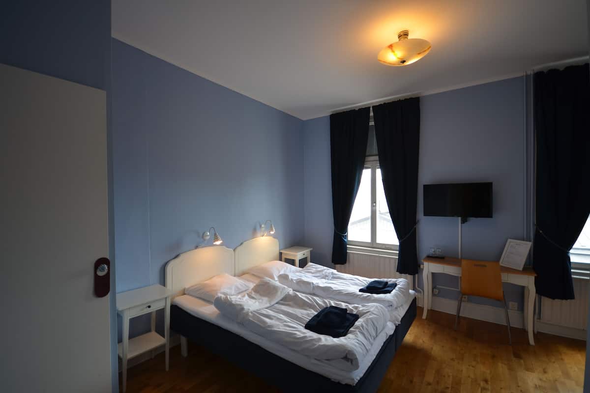 A bedroom with a bed, bedside tables, a desk, and a TV.