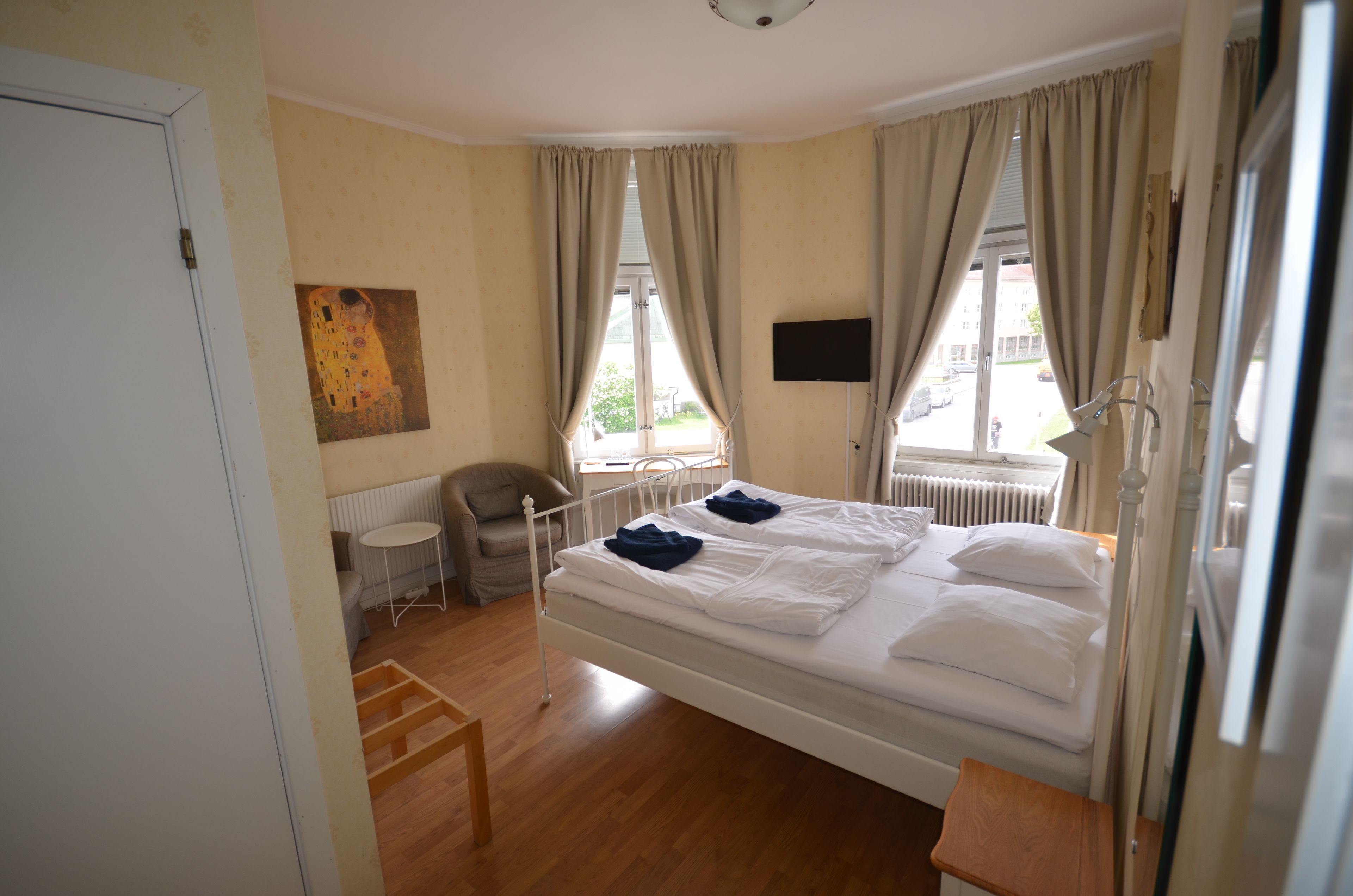 A bedroom with a single bed, a chair, a small table, a radiator, and a painting on the wall.