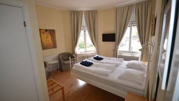 A bedroom with a single bed, a chair, a small table, a radiator, and a painting on the wall.
