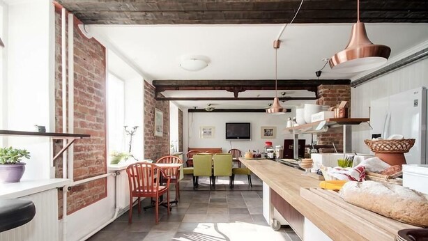 A modern kitchen with a wooden countertop, a dining area with chairs, and a brick wall. - Hotell Royal (Harnosand)