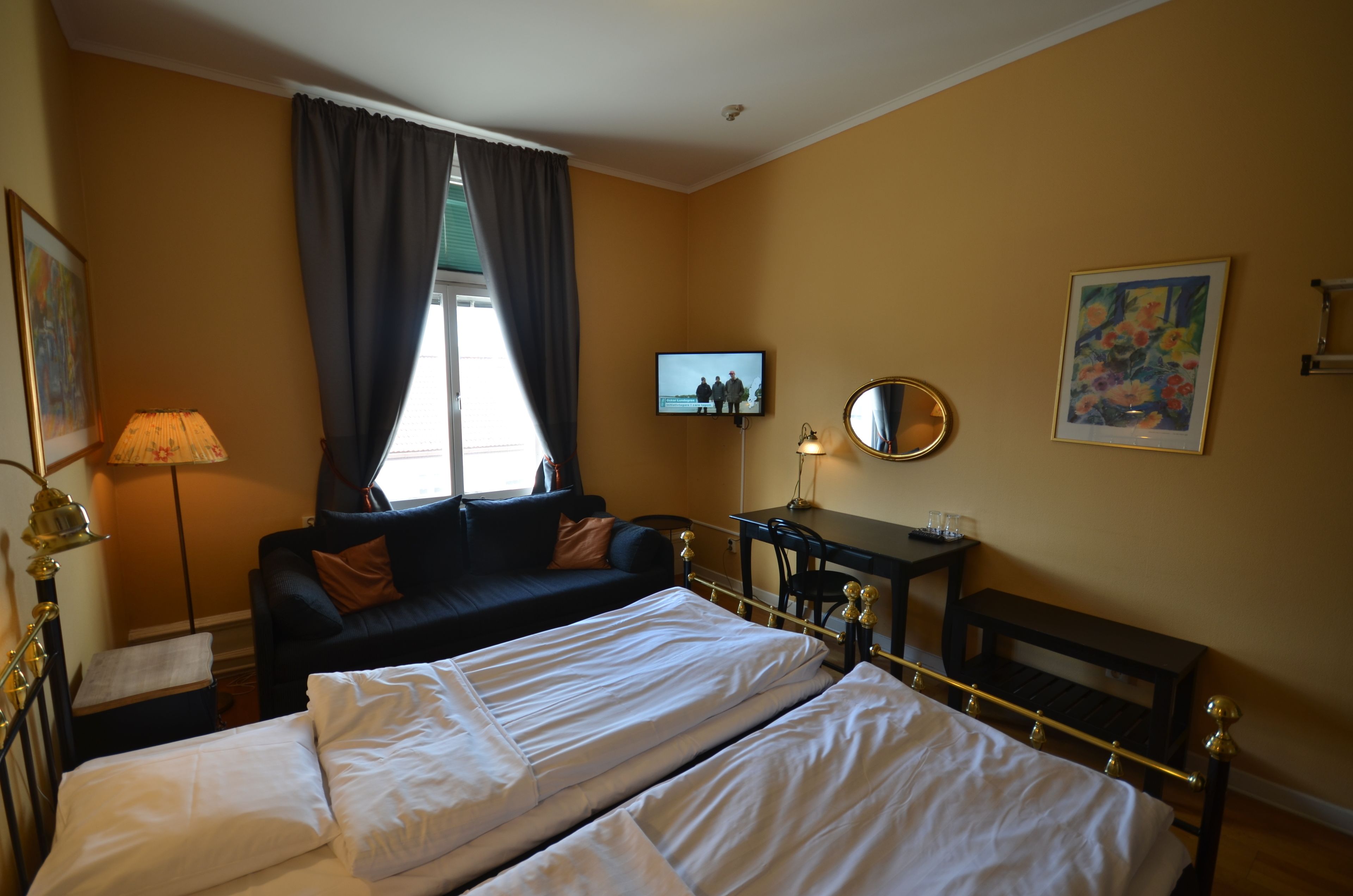 A hotel room with a bed, a sofa, a desk, a TV, and a painting on the wall.