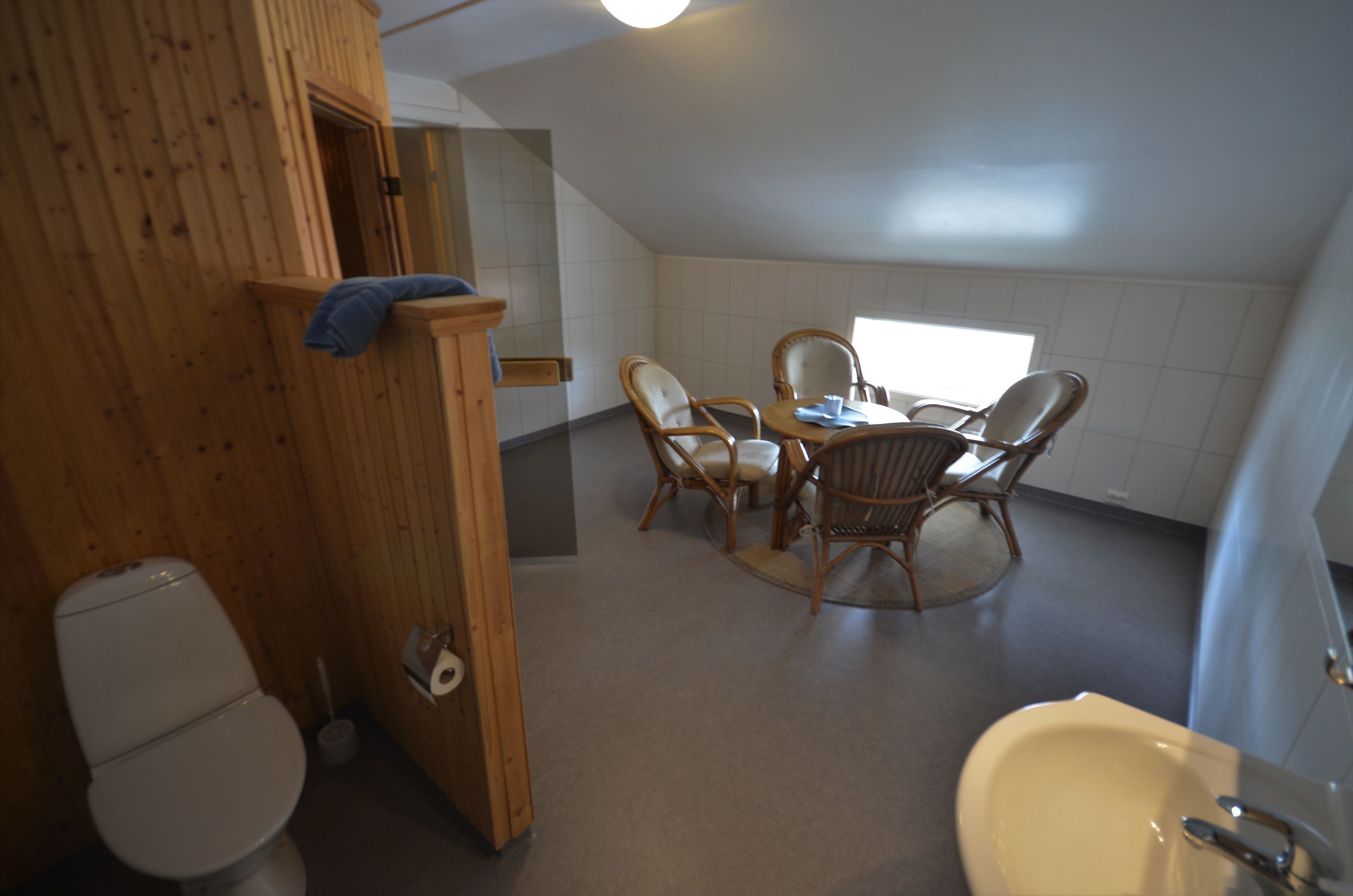 Un baño pequeño y acogedor con cabina de ducha de madera, inodoro, lavabo y una mesa redonda con cuatro sillas.