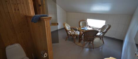 Un baño pequeño y acogedor con cabina de ducha de madera, inodoro, lavabo y una mesa redonda con cuatro sillas.