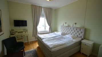 A bedroom with a bed, bedside tables, a desk, a chair, and a television.