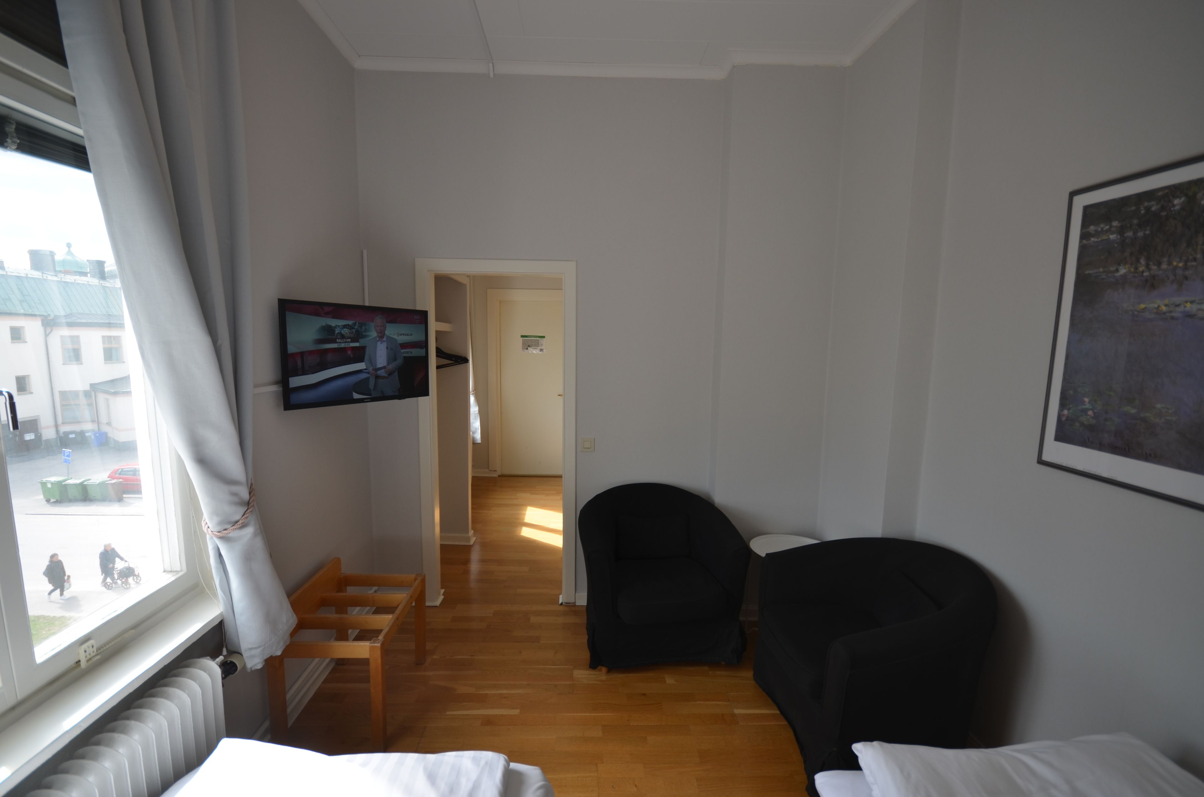 A hotel room with a wooden bench, a black armchair, a TV on the wall, and a window with curtains.