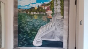 A hallway with a mural of a boat on water, a stone balustrade, and a view of houses and mountains. - Sofia and Oscar's house Lake Como Canzo (Canzo)