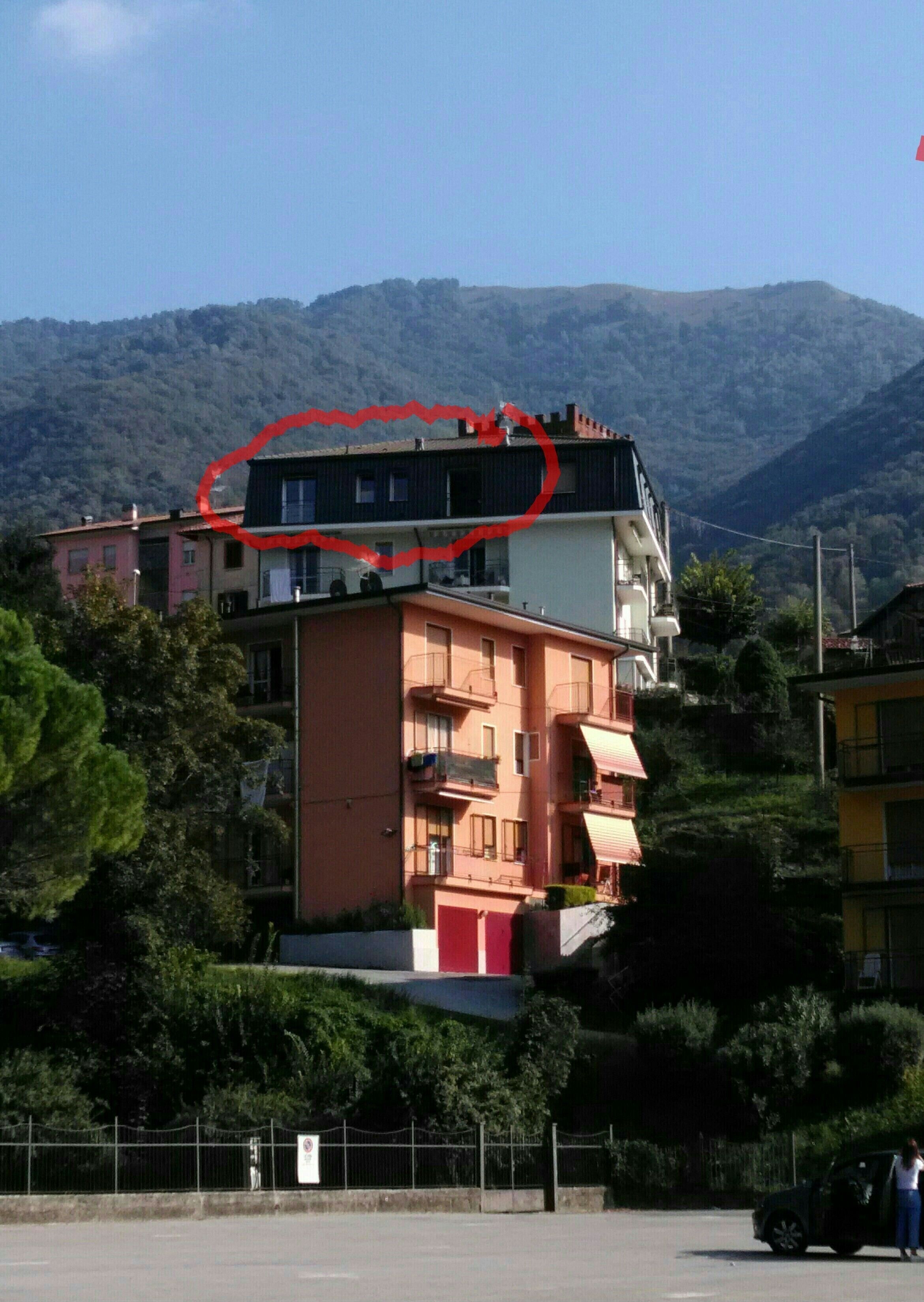 Un immeuble à plusieurs étages doté de balcons, entouré d’arbres et avec des montagnes en arrière-plan.