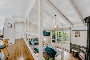 A spacious living area with a wooden floor, a sofa set, a dining table, and a fireplace. - Steep Creek Retreat (Belgrave)