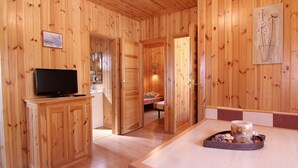 A wooden cabin interior with a television on a cabinet, a bed with a patterned bedspread, and a tray with food on a table. - Serra de Prades Resort - Campsite (Vilanova de Prades)