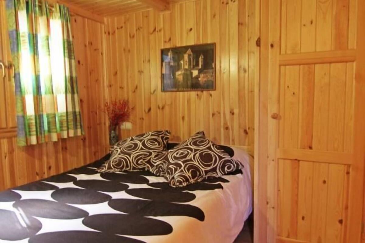 A wooden cabin room with a bed, curtains, and a painting on the wall.