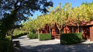 A row of wooden cabins with a gravel path leading to them, surrounded by neatly trimmed hedges and trees. - Serra de Prades Resort - Campsite (Vilanova de Prades)