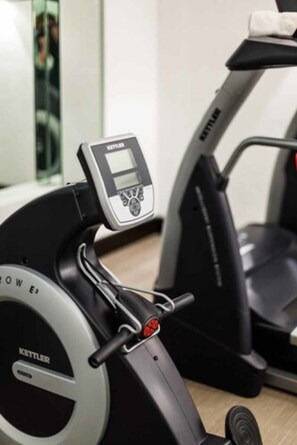 A stationary bike with a digital display and a treadmill in the background. - Hotel Künstlerquartier Seezeichen (Ostseebad Ahrenshoop)