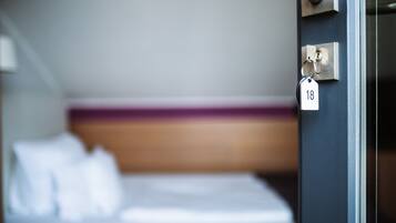 Ein Hotelzimmer mit einem Bett, einer Tür mit Schlüsselkartenverriegelung und einem Nummernschild.
