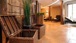 Un hall con mobiliario de mimbre, una planta grande y una zona de estar con sillas y un sofá.