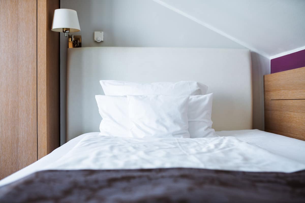 Een net opgemaakt bed met witte lakens en een donkerbruine plaid.