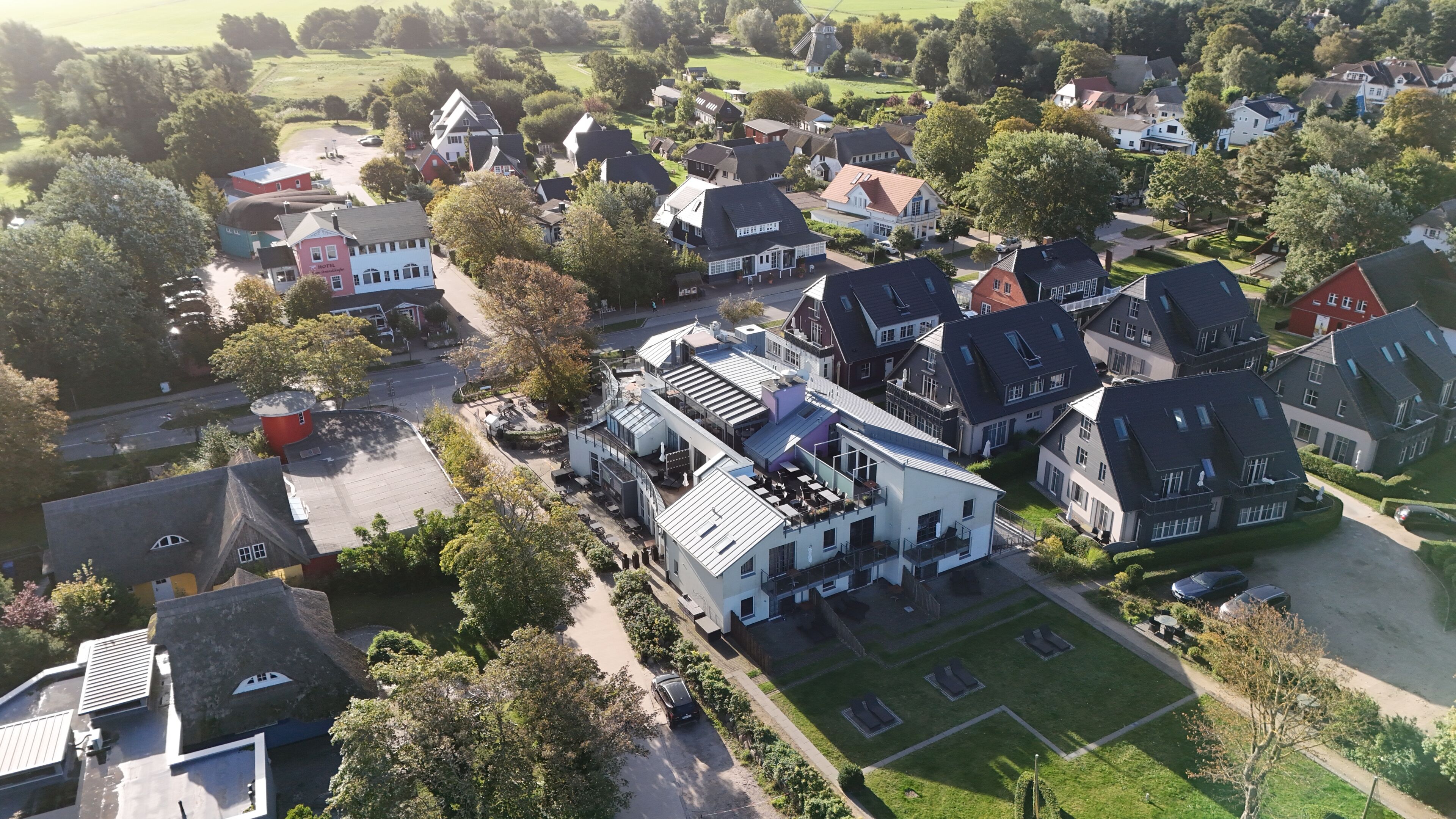 An aerial view of a residential area with houses, a windmill, and a hotel.