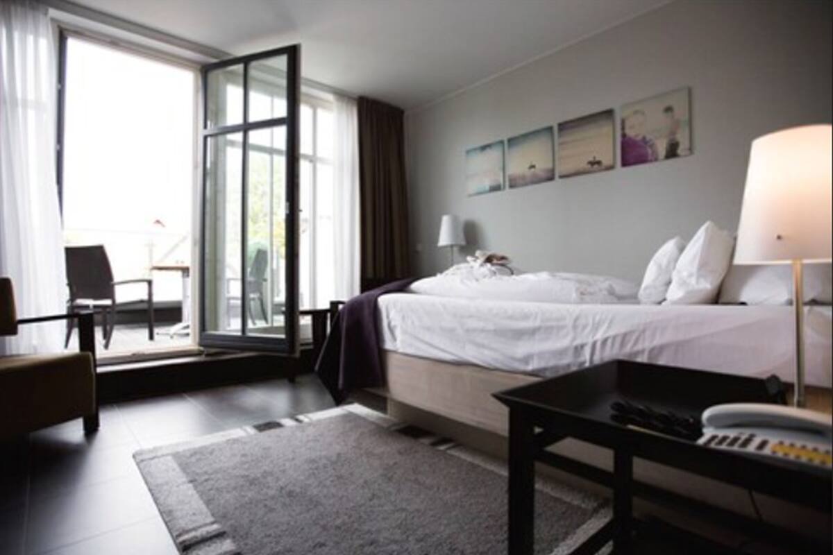 Een hotelkamer met een bed, een bureau, een stoel, een raam met gordijnen en uitzicht op de omgeving.