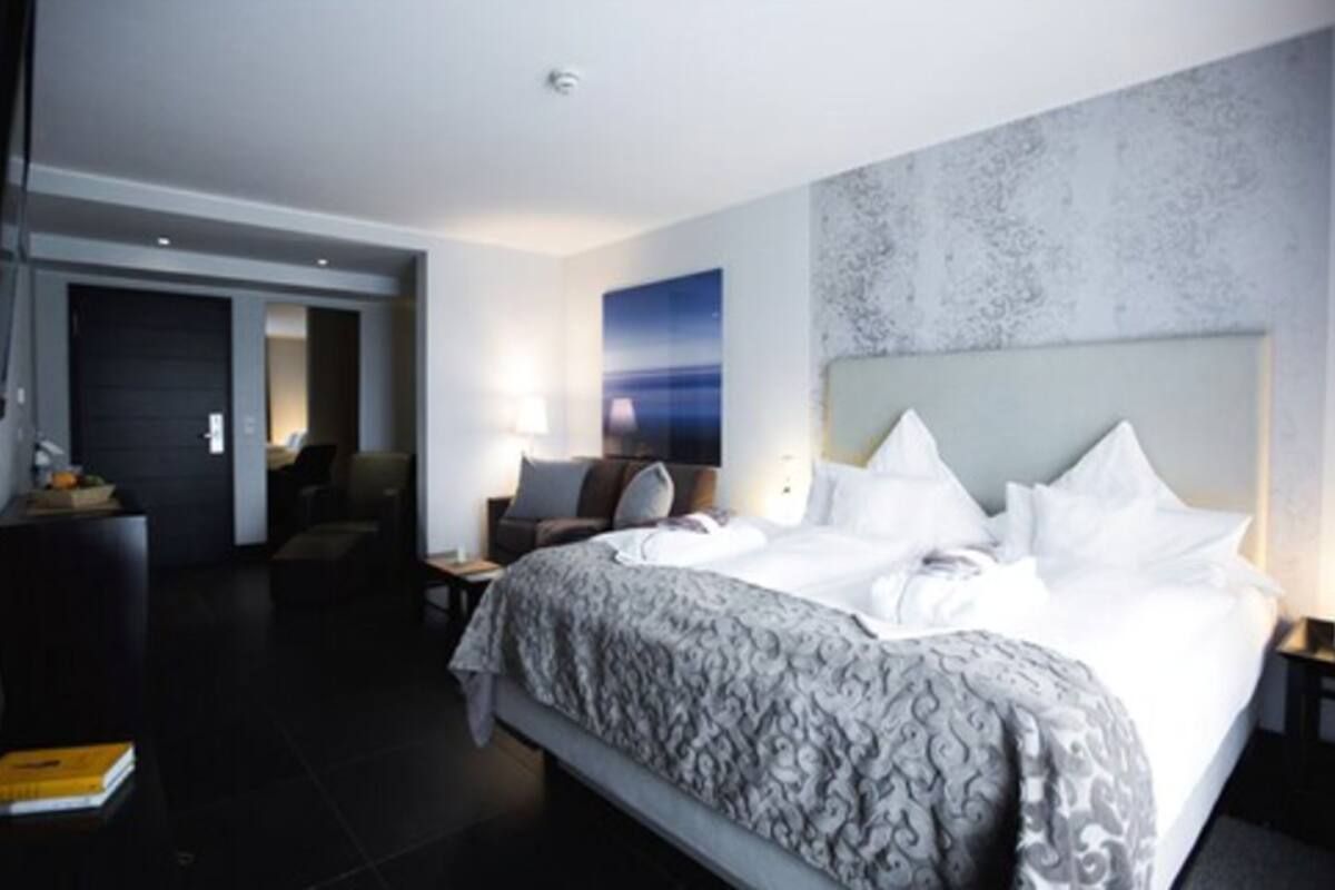 Een moderne hotelkamer met een groot bed, een bureau en een stoel. Er is een deur die naar een andere kamer leidt, en een muur met een structuur.