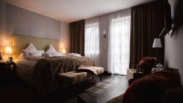Ett hotellrum med en stor säng, ett nattduksbord med en lampa, en stol och ett skrivbord med en lampa.
