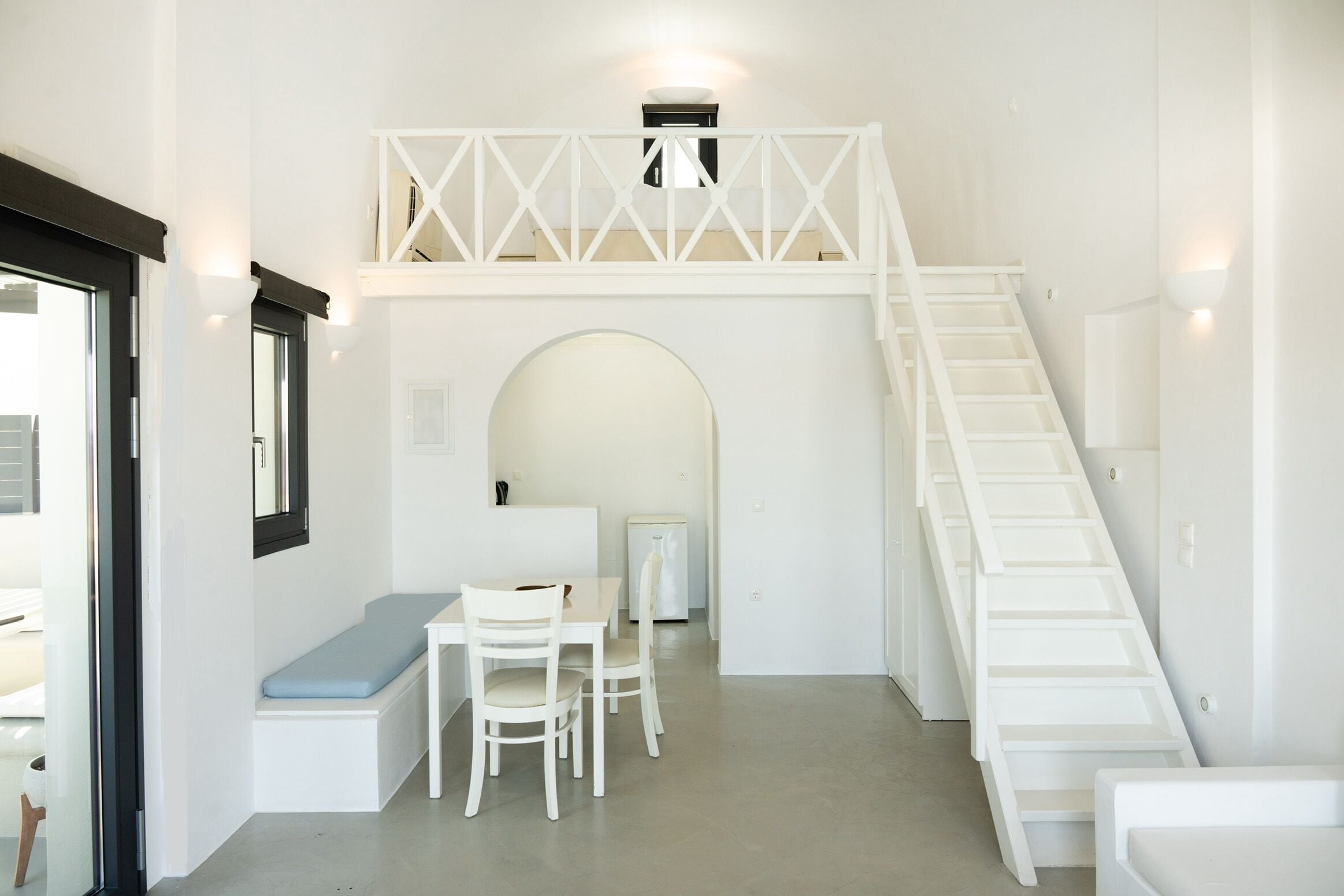 Un interior moderno con una escalera blanca, un banco y un área de comedor.