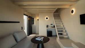 Een moderne woonkamer met een bank, een ronde salontafel, een trap en een keukenhoek.