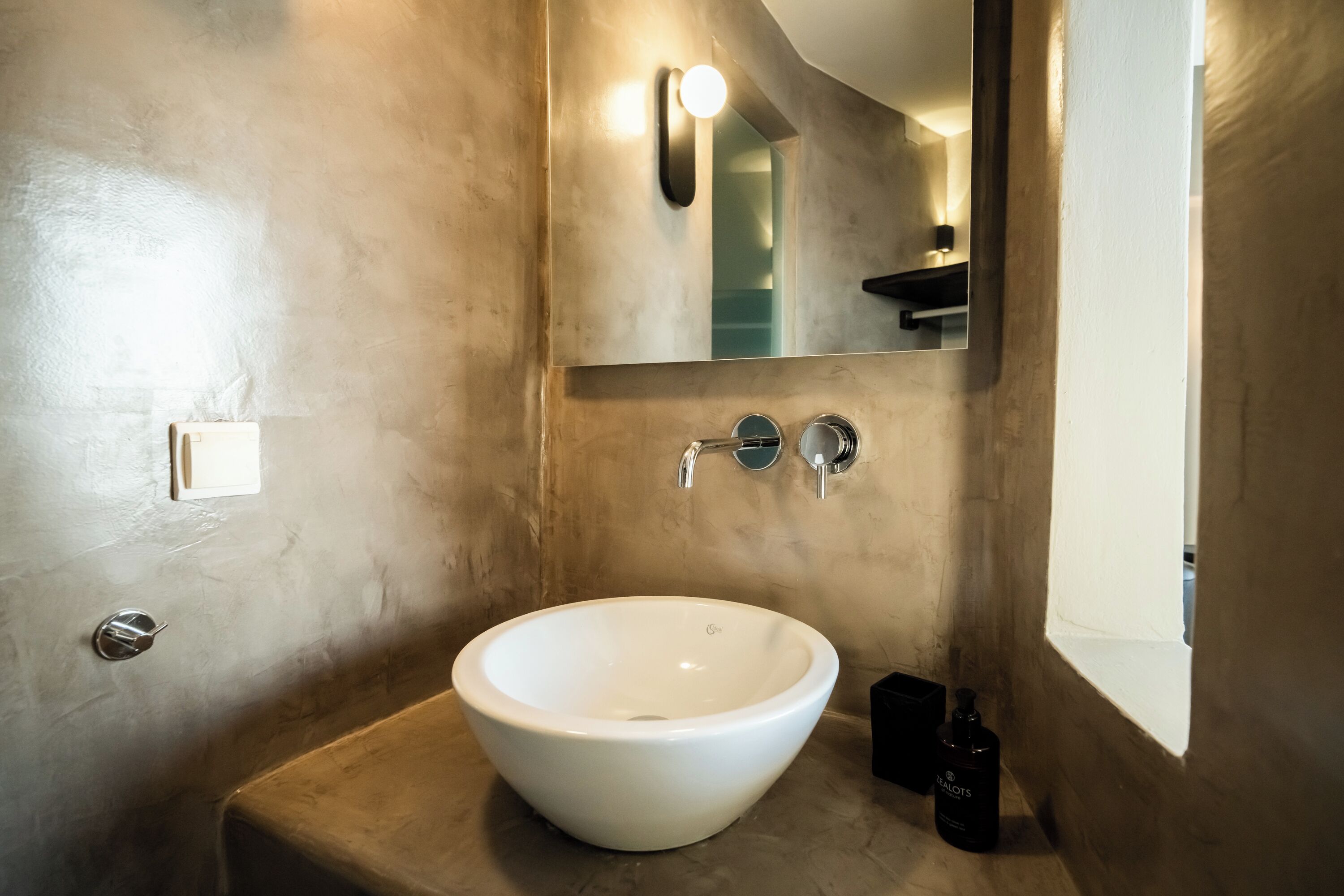 A bathroom with a large white sink, a mirror, and a light fixture above the mirror.