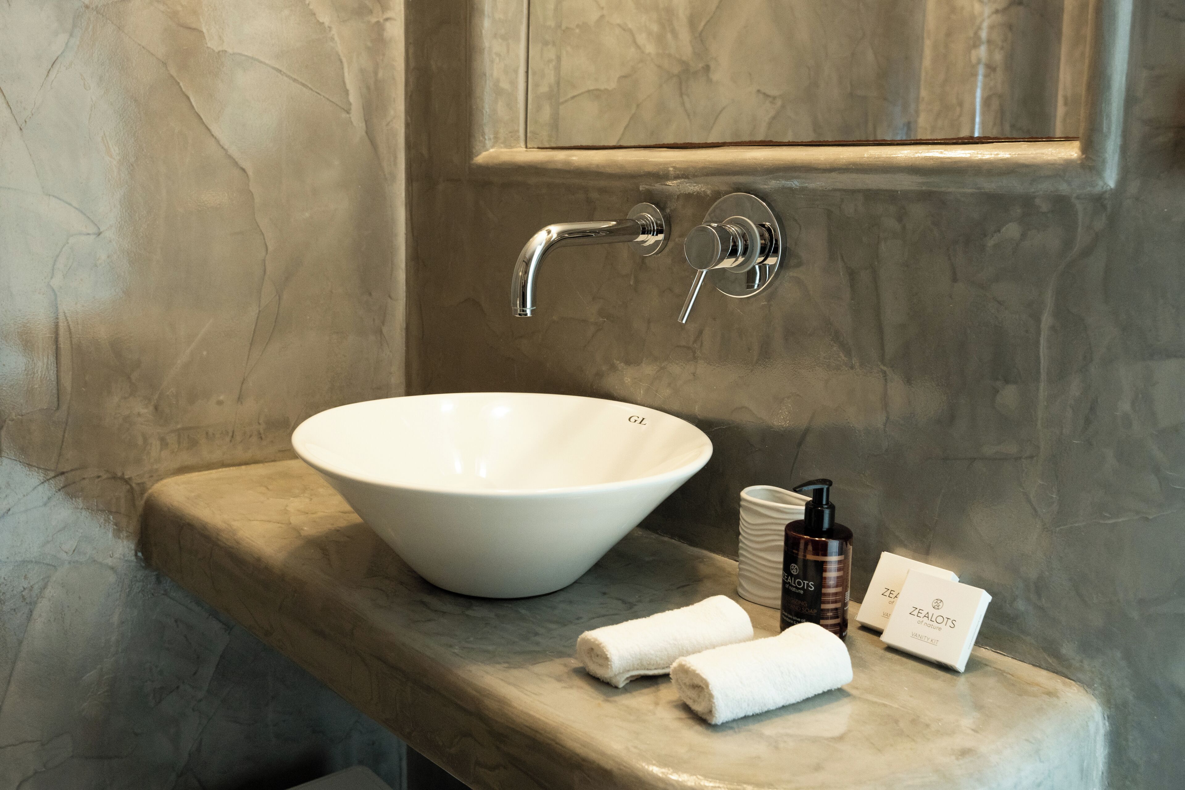 A bathroom with a white basin, a towel, and toiletries on a marble countertop.