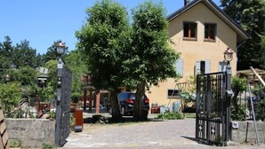 Ein gepflasterter Weg führt zu einem Haus mit einem Tor, umgeben von Bäumen und einem geparkten Auto.