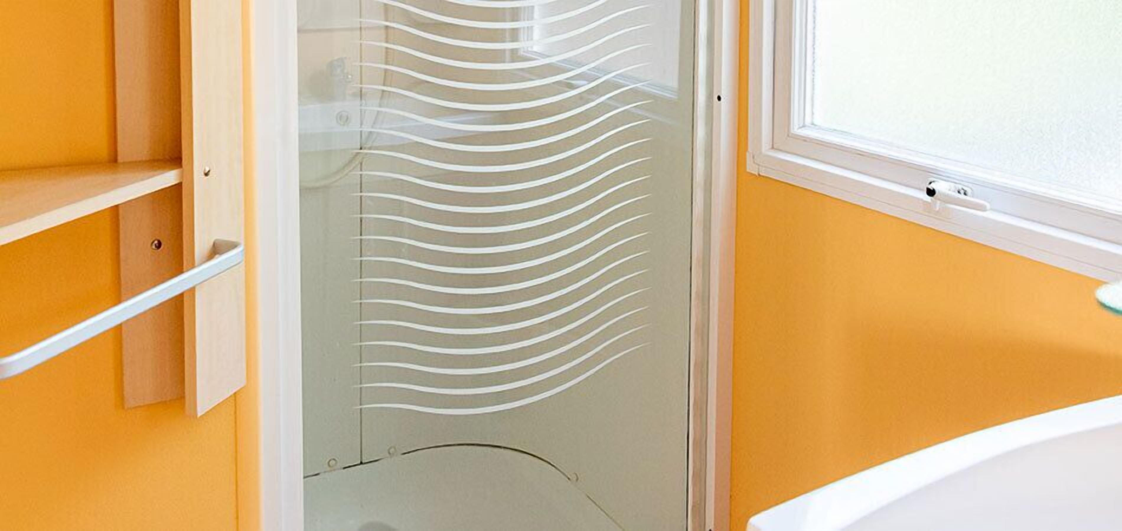 Un bagno con porta in vetro, una vasca da bagno bianca e un parete gialla.