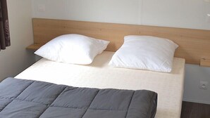A bed with a wooden headboard, two white pillows, and a grey duvet. - Camping L'évasion - Mobilhomes (Puy-l'Eveque)