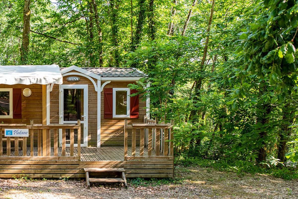 A wooden cabin with a porch, surrounded by dense forest.