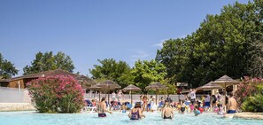 Área de piscina com espreguiçadeiras e guarda-sóis, cercada por árvores e uma grade.