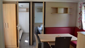 A compact room with a kitchenette, a dining area, and a red sofa. - Camping L'évasion - Mobilhomes (Puy-l'Eveque)
