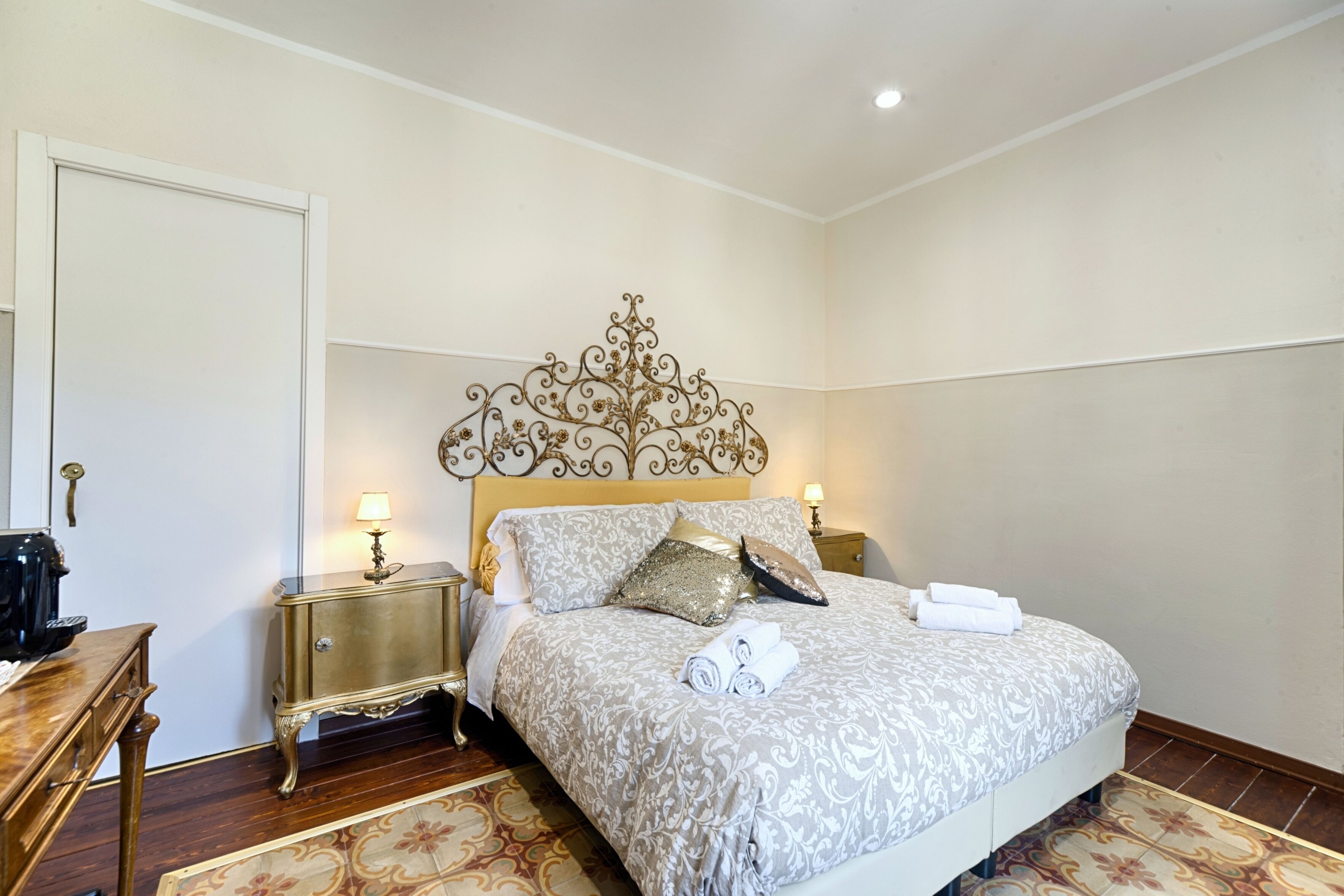 A neatly arranged bedroom with a large bed, bedside tables, a dresser, and a mirror.