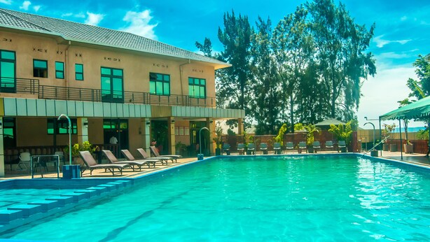 A swimming pool with lounge chairs and a building with multiple windows and balconies. - Hotel Hilltop Country Club (Kigali)