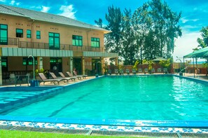 A swimming pool with lounge chairs and a building with multiple windows and balconies. - Hotel Hilltop Country Club (Kigali)